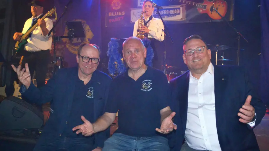 Freude über eine gelungene 20. Lions Blues Party bei (v.l.): Rüdiger Claußen, Thomas Schönhoff (Organisatoren) und Sebastian Koch (Präsident „Lions Club Itzehoe“) vor der Bühne mit der Itzehoer Blues Band „Die Blaue Stunde“ (hinten).